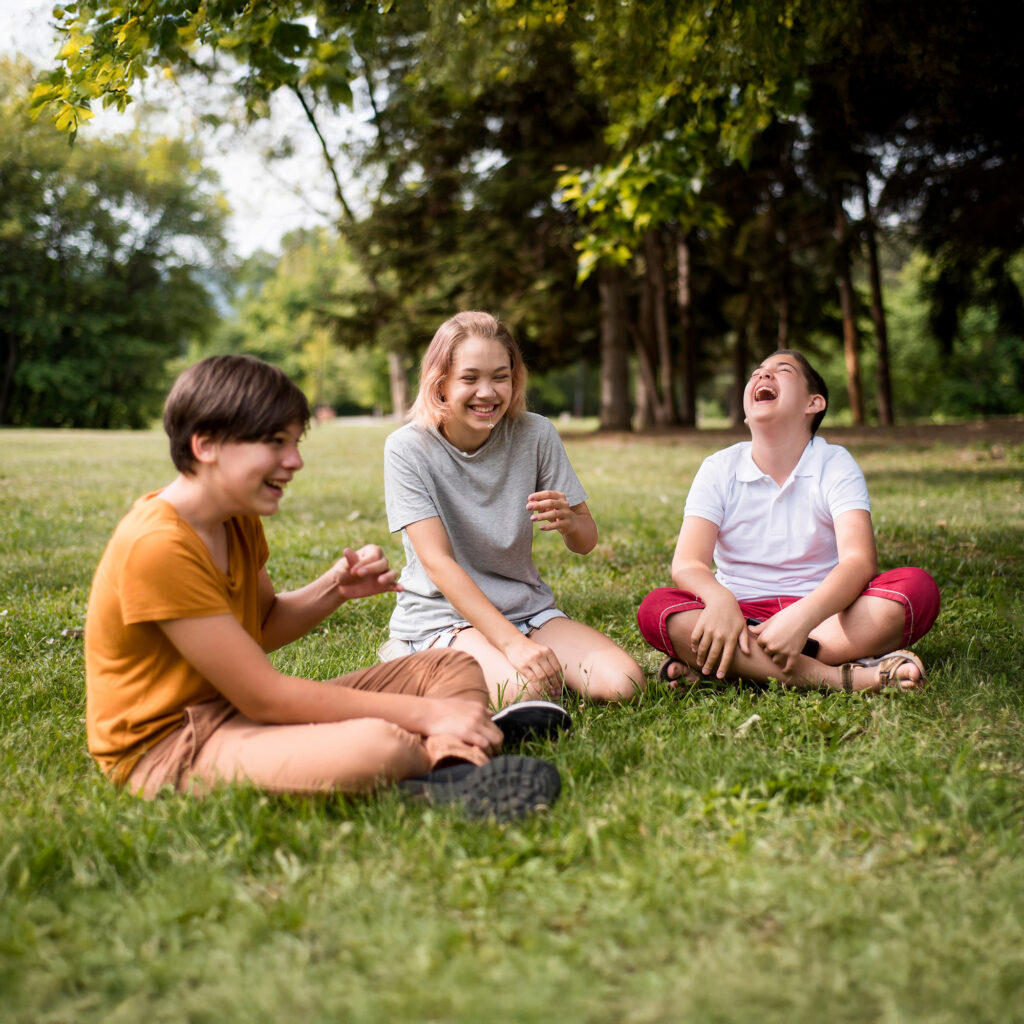 Drei Kinder sitzen auf einer Wiese und haben Spaß zusammen