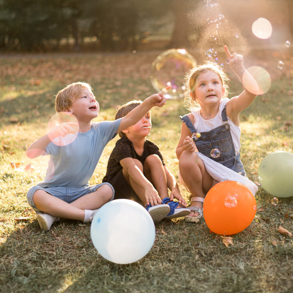 Drei Kinder sitzen auf einer Wiese und spielen mit Seifenblasen
